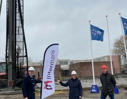 Drie personen staan op een bouwplaats bij de vlag van Intermaris