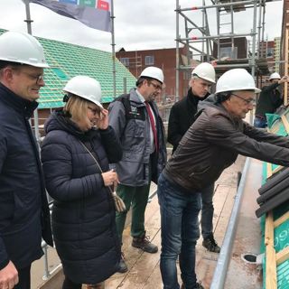 Verschillende mensen met een bouwhelm op staan op het dak en leggen dakpannen