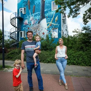 Man met kinderen en medewerker Intermaris staan voor een woongebouw met een muurschildering