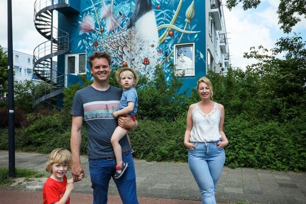Man met kinderen en medewerker Intermaris staan voor een woongebouw met een muurschildering