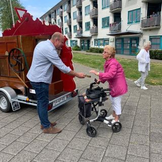 Bewoonster met rollator geeft geld aan de man van de draaiorgel