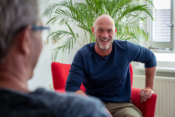 Medewerker van Intermaris zit lachend op een rode stoel in gesprek met een bewoner