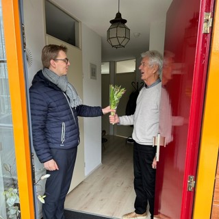 Bewoner ontvangt een bos tulpen van directeur wonen Jurre Terhorst tijdens complimentendag