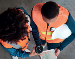 Twee personen met een oranje hesje aan bespreken een plan