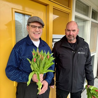 Bewoner en medewerker Intermaris poseren voor woning met een bos tulpen