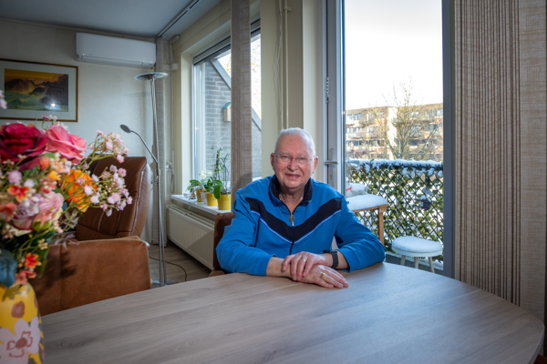 Bewoner met blauw jack aan zit aan tafel in zijn appartement